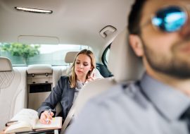 Business woman with smartphone sitting on back seat in taxi car, talking on the phone.