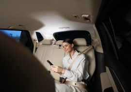 A woman sitting in a car's back seat, concentrating on her cell phone, displaying a moment of modern connectivity and focus.